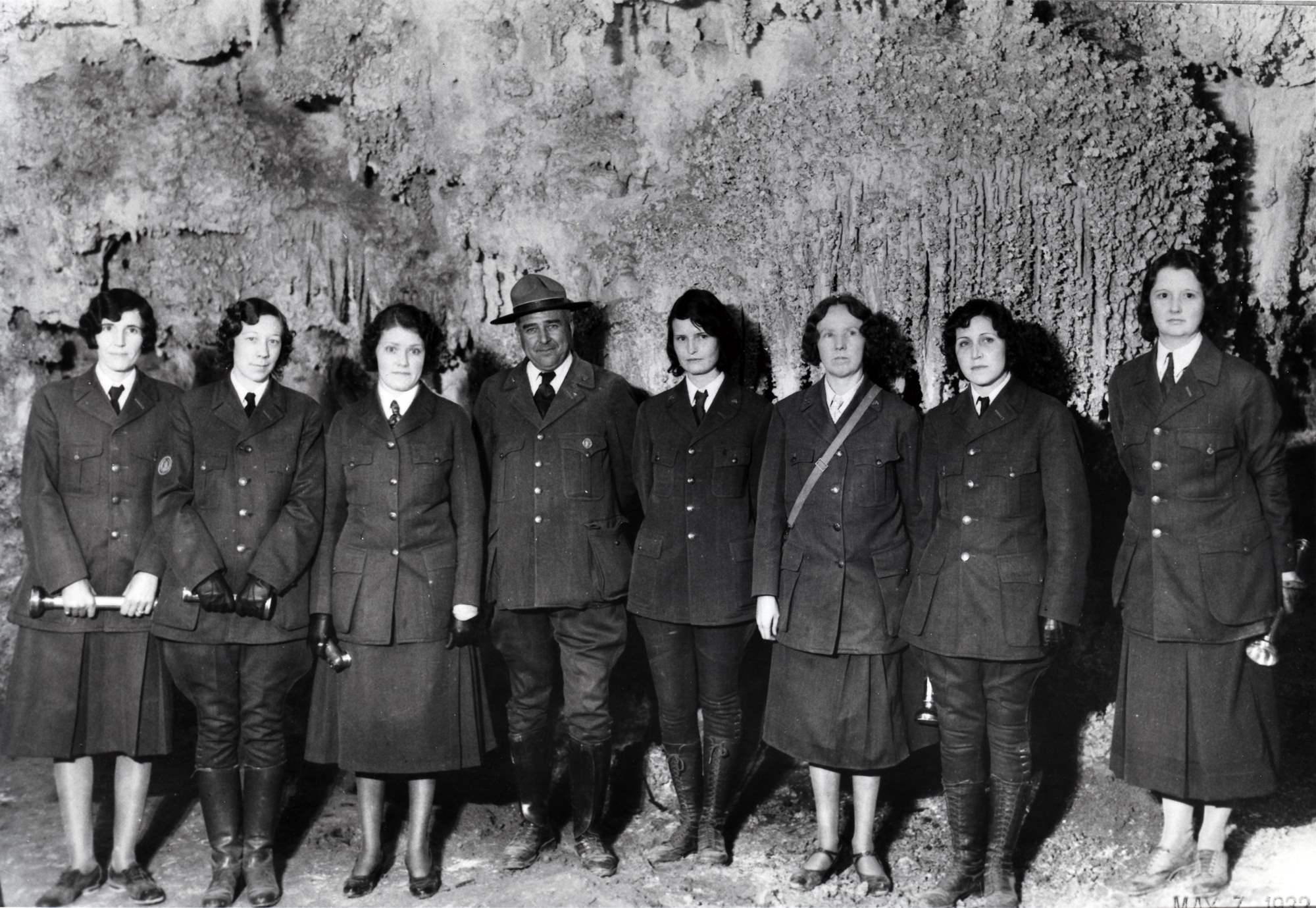 Seven women pose with Thomas Boles inside a cave. They all wear NPS uniforms. Only Boles wears a broad brim hat and a round superintendent’s badge.